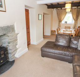 A living room with a brown leather sofa a stone fireplace and a dining table with chairs at Goswick Hall in Bowland Bridge