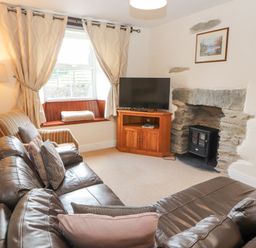 A living room with a leather sofa armchair lamp TV and stone fireplace at Goswick Hall Bowland Bridge