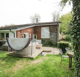 A backyard with a hot tub on a wooden deck chairs and a table next to a house with wood and stone exterior at Lake Lodge in Bowness-On-Windermere