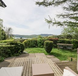 An outdoor patio area with chairs table and hot tub overlooking garden shrubs and distant hills at Lake Lodge in Bowness-On-Windermere