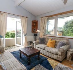 A living room with two plaid sofas and a wooden coffee table next to large windows and a sliding glass door at Lake Lodge in Bowness-On-Windermere