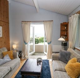 A sitting room with two sofas and a wooden coffee table in front of open patio doors at Lake Lodge in Bowness-On-Windermere