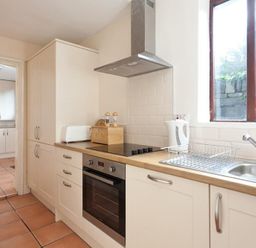 A kitchen with white cabinets a stove oven sink and a window at Honeysuckle Cottage in Bowness