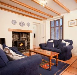A living room with two blue sofas a wooden coffee table a fireplace and wooden beams at Honeysuckle Cottage in Bowness