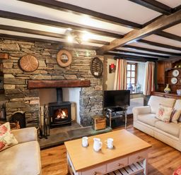 A living room with a stone fireplace wooden beams and two beige sofas at Gunpowder Cottage in Langdale