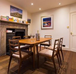 A dining room with a wooden table and six chairs and a fireplace with books on the mantelpiece at Orrest Range in Windermere