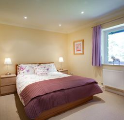 A bedroom with a double bed two bedside tables with lamps a window with purple curtains and a radiator at The Old Barn in Ambleside