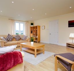 A living room with beige sofas, striped cushions, a wooden coffee table, a bookshelf, and a chair at The Old Barn in Ambleside