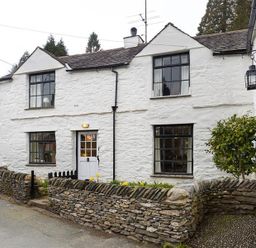 A white stone cottage with black window frames and a small stone wall garden at Camellia Cottage in Bowness