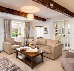 A living room with sofas armchairs a wooden coffee table and exposed wooden beams at Camellia Cottage in Bowness