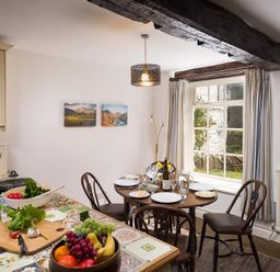 A kitchen and dining area with a round table set for four near a window and a countertop with fruit and vegetables at Camellia Cottage in Bowness