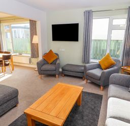 A living room with gray armchairs and a wooden coffee table next to a dining area at Bowderstone in Keswick