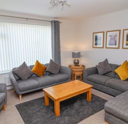 A living room with gray sofas and chairs yellow cushions a wooden coffee table and framed pictures on the wall at Bowderstone in Keswick