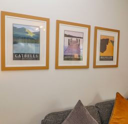 Three framed posters of Catbells Derwentwater and Helvellyn above a grey sofa with cushions at Bowderstone in Keswick