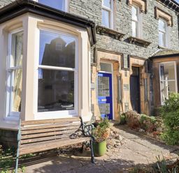 A stone house exterior with bay windows a blue door and a wooden bench with plants outside at Number Twenty in Keswick