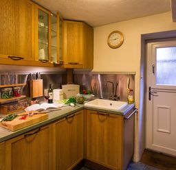 A kitchen with wooden cabinets a countertop with vegetables a sink and a door at Burrow Cottage in Bowness