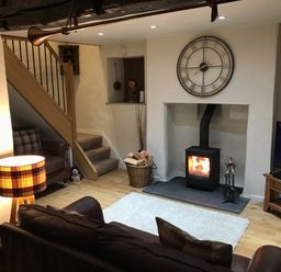 A living room with a wood burning stove and a large clock above it at Burrow Cottage in Bowness