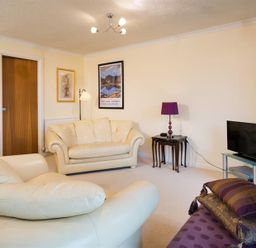 A living room with cream leather sofas a purple lamp a TV on a glass stand and framed pictures on the walls at Mount Sol in Ambleside