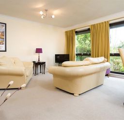 A living room with cream sofas a black TV a purple lamp a dining table with chairs and large windows with yellow curtains at Mount Sol in Ambleside
