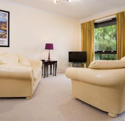 A living room with two cream sofas a small black table with a purple lamp a television and yellow curtains at Mount Sol in Ambleside