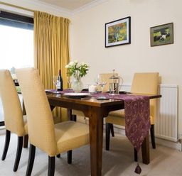 A dining room with a wooden table set with glasses and a vase of flowers at Mount Sol in Ambleside