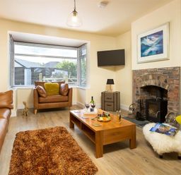 A living room with leather sofas a wooden coffee table a brick fireplace and a window at Greengarth in Keswick