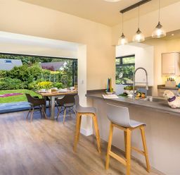 A kitchen with a breakfast bar and stools next to a dining table by a garden at Greengarth in Keswick