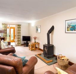 A living room with leather sofas a wood stove a TV and a basket of firewood at Garden Cottage At Coniston in Coniston