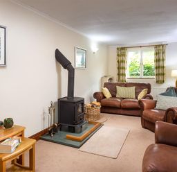 A living room with leather sofas a wood burning stove and side tables at Garden Cottage At Coniston in Coniston