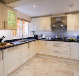 A kitchen with beige cabinets black countertops a stove with pots a microwave and a sink with a window at Garden Cottage At Coniston in Coniston