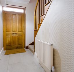 An entryway with a wooden front door a carpeted staircase and a wall-mounted radiator at Pippin Cottage in Keswick