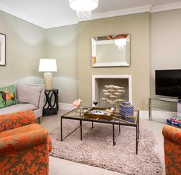 A living room with patterned orange chairs a glass coffee table a gray sofa and a television at Pippin Cottage in Keswick