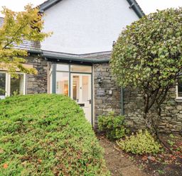 The entrance to a stone cottage with a white door and surrounding plants at Pudding Cottage in Ambleside