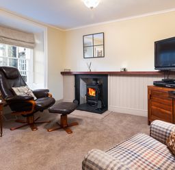 A living room with a leather chair and footstool a fireplace and a television at Ghyll Foot Cottage in Ambleside