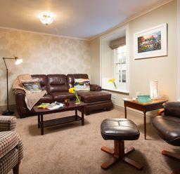 A living room with leather sofa and armchair a coffee table and side table with books and flowers at Ghyll Foot Cottage Ambleside