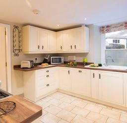 A kitchen with white cabinets a microwave a toaster a sink and vegetables on the counter at Ghyll Foot Cottage Ambleside
