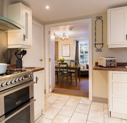 A kitchen with a stove a pot and kitchen utensils and a counter with bread leading to a dining area with a table and chairs at Ghyll Foot Cottage in Ambleside