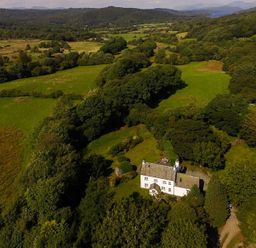 An aerial view of a white house surrounded by trees and green fields at Fair Rigg Old Farm in Cartmel