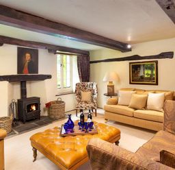 A living room with a fireplace two sofas an armchair and a large ottoman with a tray of bottles and glasses at Fair Rigg Old Farm in Cartmel