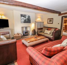 A living room with three sofas a wood burning stove a television and wall art at Low Cartmell Fold in Crosthwaite