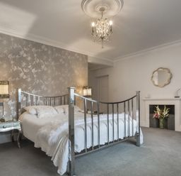 A bedroom with a metal bed frame bedside tables lamps wallpaper and a fireplace with flowers at Tent Lodge in Coniston