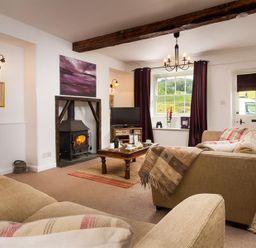 A living room with beige sofas a wood burning stove and a window with curtains at Pollys Cottage in Langdale
