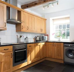 A kitchen with wooden cabinets a washing machine an oven a microwave and a window at Pollys Cottage in Langdale