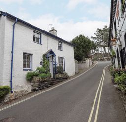A narrow street with white buildings and plants along the sides at Springwell Cottage in Ambleside