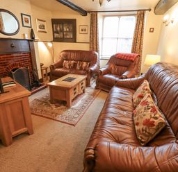 A living room with brown leather sofas a wooden coffee table a fireplace and a television at Springwell Cottage in Ambleside