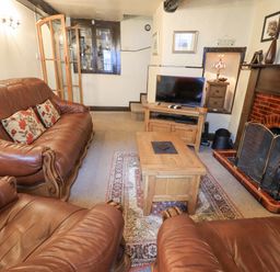 A living room with brown leather sofas a wooden coffee table television and a fireplace at Springwell Cottage in Ambleside