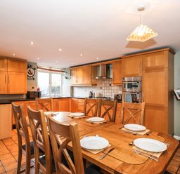 A kitchen with wooden cabinets a dining table set with plates and cutlery and a stand with open books at Candleberry Cottage in Ambleside