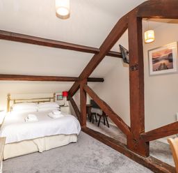 A bedroom with a bed and bedside tables under a sloped ceiling with exposed wooden beams at Candleberry Cottage in Ambleside
