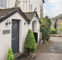 Exterior view of a white cottage with a dark door and small trees near the entrance at Gale Lodge Cottage in Ambleside