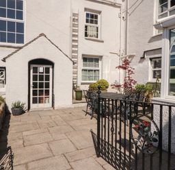 An outdoor patio area with a black metal table and chairs next to white buildings at Gale Lodge Cottage in Ambleside